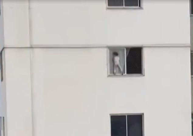 Criança brinca em janela do 4º andar, apoiada só por uma tela